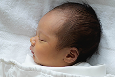 Head and shoulders view of a newborn sleeping under a white cover
