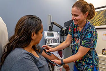 A smiling nurse outs a blood pressure cuff on the left arm of patient seated in a treatment chair in a medical exam room