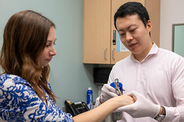 A dermatologist holds a patient’s arm while examining the skin on their wrist with a clinical tool