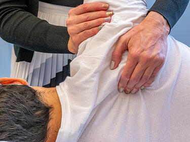 Closeup view of a clinician‘s hands performing and orthopedic adjustment of a patient’s should as they lie on their left side.